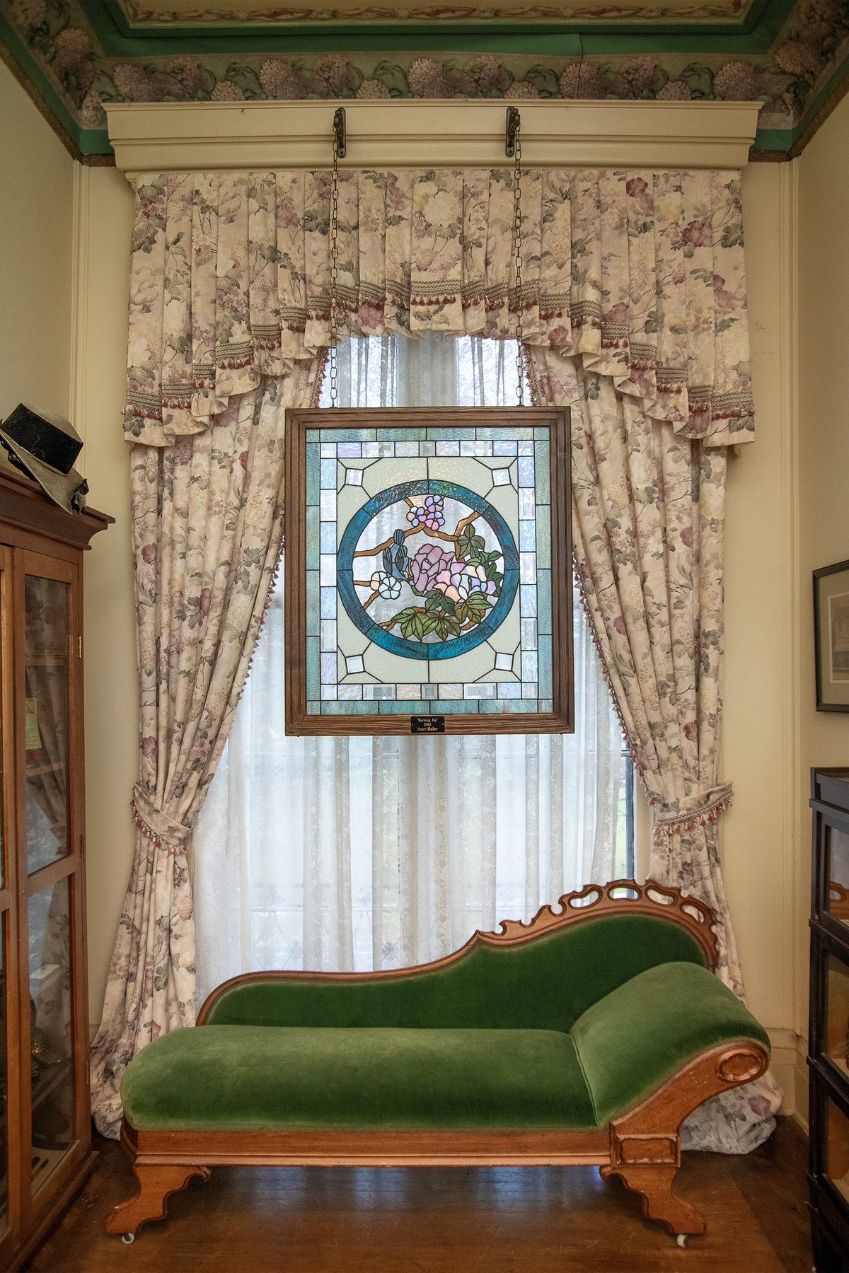 A stained-glass window and fainting couch inside the Long Home Museum